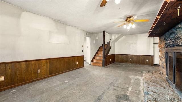 unfurnished living room with ceiling fan, a textured ceiling, a fireplace, and wood walls