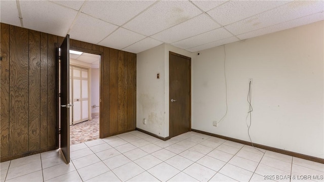 empty room featuring a drop ceiling and wood walls