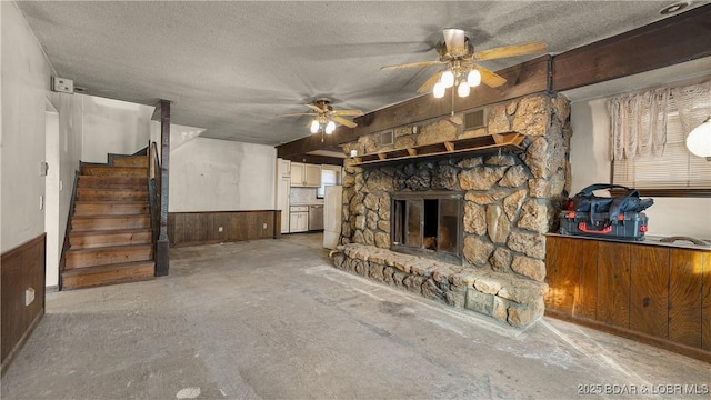 unfurnished living room with ceiling fan, a fireplace, a textured ceiling, and wood walls