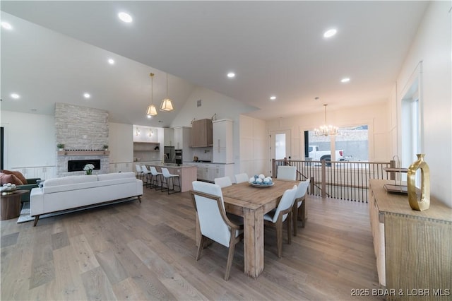 dining room with vaulted ceiling, a notable chandelier, light hardwood / wood-style floors, and a fireplace