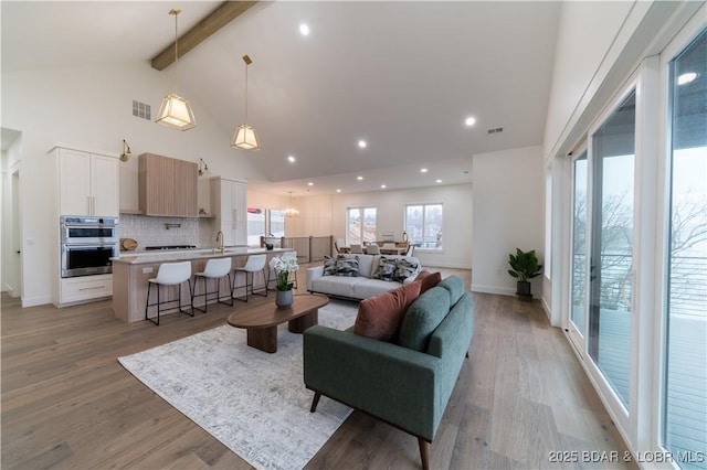 living room with sink, high vaulted ceiling, beam ceiling, and light hardwood / wood-style floors