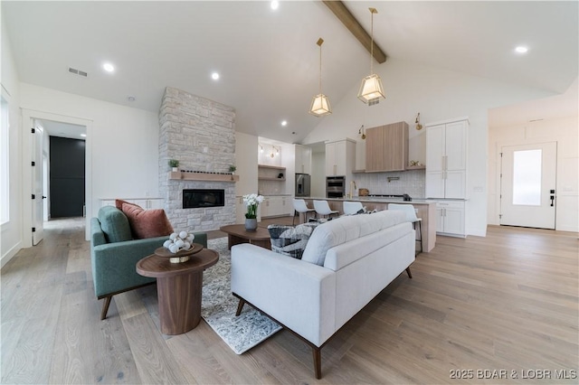 living room featuring beamed ceiling, a stone fireplace, high vaulted ceiling, and light hardwood / wood-style flooring