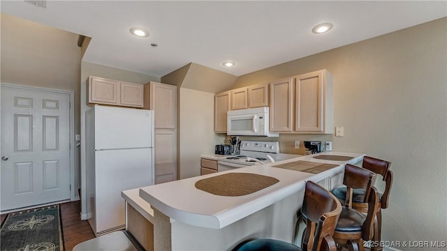 kitchen with a breakfast bar area, light brown cabinets, dark hardwood / wood-style floors, kitchen peninsula, and white appliances