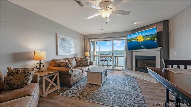 living room featuring ceiling fan, a high end fireplace, and wood-type flooring