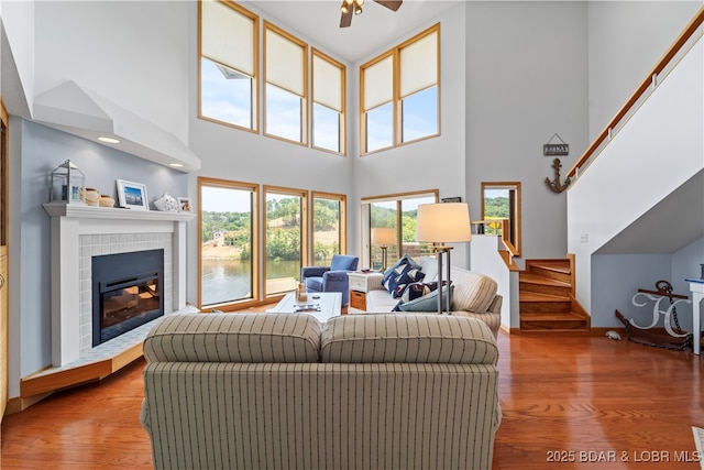 living room featuring a towering ceiling, hardwood / wood-style floors, a fireplace, ceiling fan, and a water view