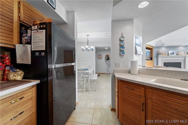 kitchen with stainless steel refrigerator, decorative light fixtures, sink, light tile patterned floors, and an inviting chandelier