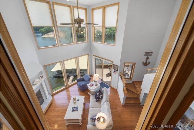 living room with ceiling fan, a fireplace, light hardwood / wood-style flooring, and a high ceiling