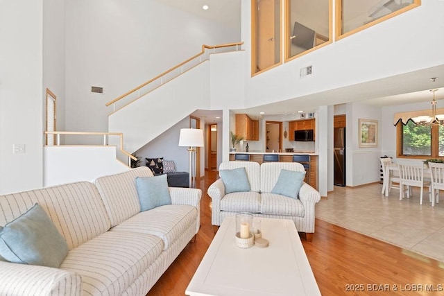 living area with a towering ceiling, stairway, light wood finished floors, and a chandelier