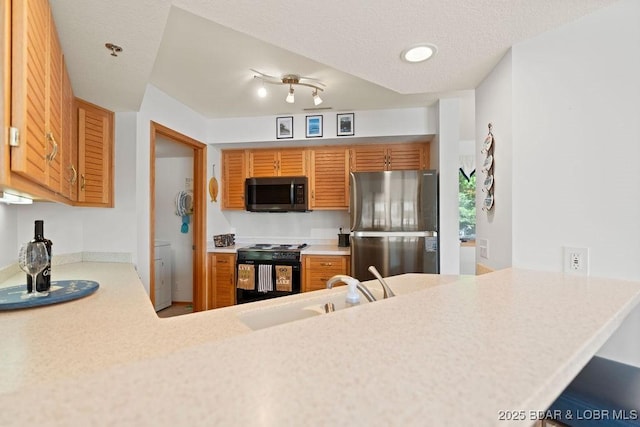 kitchen with black range oven, freestanding refrigerator, a sink, light countertops, and brown cabinetry