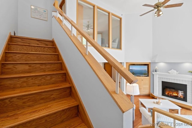 staircase with a ceiling fan, wood finished floors, and a fireplace