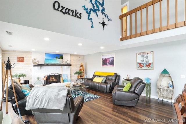 living room with hardwood / wood-style flooring, a brick fireplace, and a towering ceiling