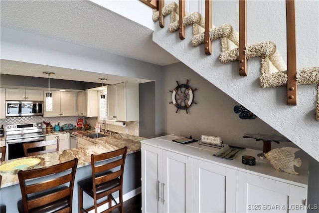 kitchen featuring appliances with stainless steel finishes, pendant lighting, sink, white cabinets, and backsplash