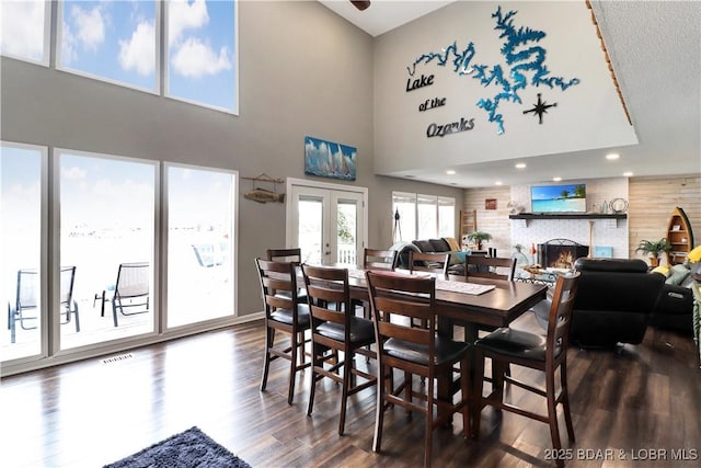 dining space featuring french doors, a towering ceiling, dark hardwood / wood-style floors, and a brick fireplace