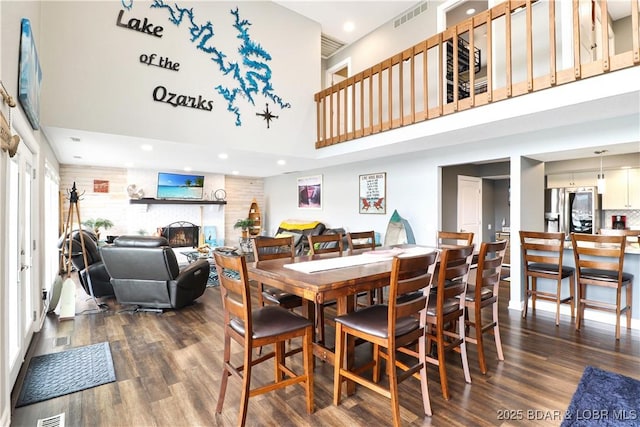 dining room with a towering ceiling, a fireplace, and dark hardwood / wood-style floors