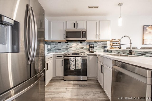 kitchen with appliances with stainless steel finishes, tasteful backsplash, white cabinetry, sink, and hanging light fixtures