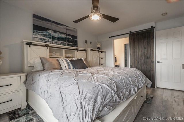 bedroom featuring dark hardwood / wood-style floors, ceiling fan, and a barn door