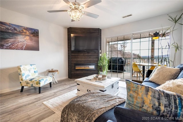 living room featuring a fireplace, ceiling fan, and light wood-type flooring