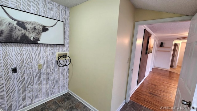 laundry room featuring hookup for a washing machine, an accent wall, wallpapered walls, baseboards, and stone finish floors