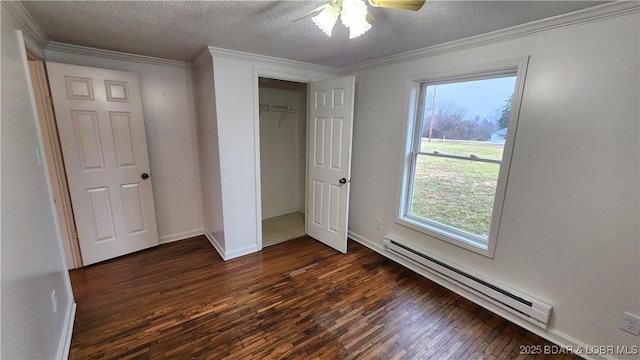 unfurnished bedroom featuring a baseboard heating unit, dark wood finished floors, a textured ceiling, ornamental molding, and multiple windows