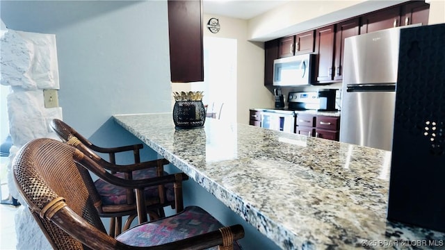 kitchen with light stone counters, stainless steel appliances, kitchen peninsula, and a kitchen bar