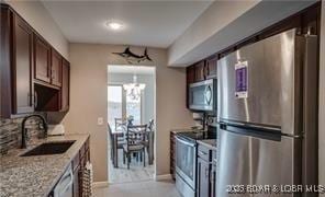 kitchen featuring appliances with stainless steel finishes, sink, a notable chandelier, light stone counters, and dark brown cabinets