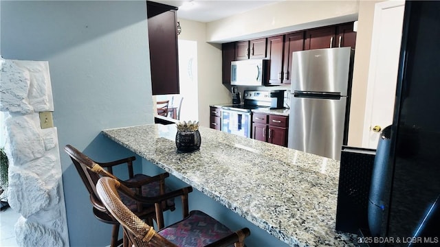 kitchen with stainless steel appliances, light stone countertops, kitchen peninsula, and a breakfast bar area