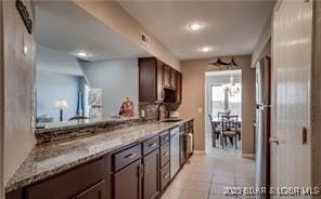 kitchen featuring sink, dark brown cabinets, light tile patterned floors, light stone countertops, and backsplash