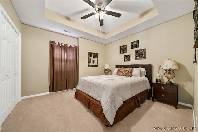 bedroom with light carpet, a tray ceiling, a closet, and ceiling fan