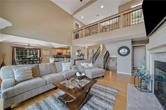 living room with a tile fireplace, a towering ceiling, ceiling fan, and light hardwood / wood-style flooring