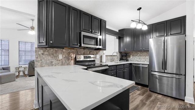 kitchen featuring vaulted ceiling, appliances with stainless steel finishes, decorative light fixtures, sink, and dark wood-type flooring