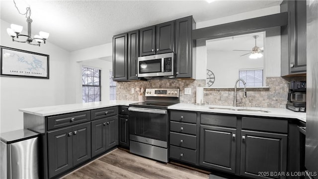 kitchen featuring sink, vaulted ceiling, appliances with stainless steel finishes, kitchen peninsula, and hardwood / wood-style flooring