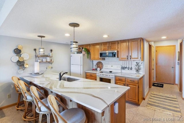 kitchen featuring sink, a breakfast bar area, hanging light fixtures, kitchen peninsula, and white appliances