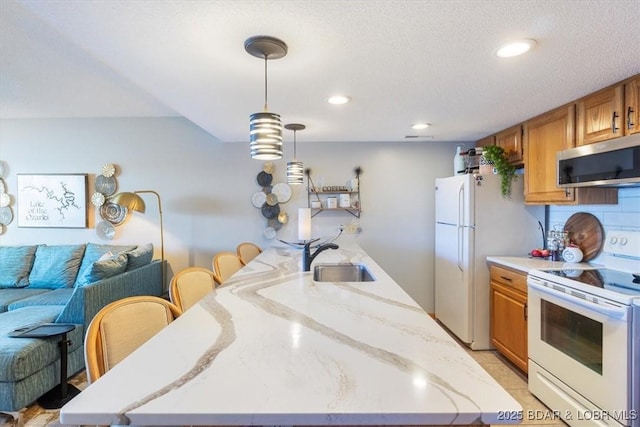 kitchen featuring a kitchen bar, sink, decorative light fixtures, white appliances, and backsplash