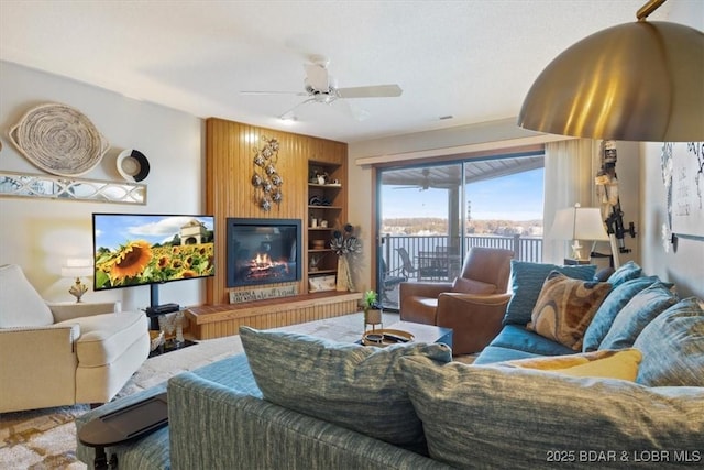 living room featuring ceiling fan, a fireplace, and built in shelves