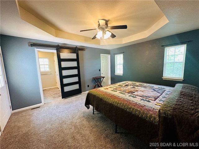 bedroom featuring a raised ceiling, a barn door, carpet floors, and multiple windows