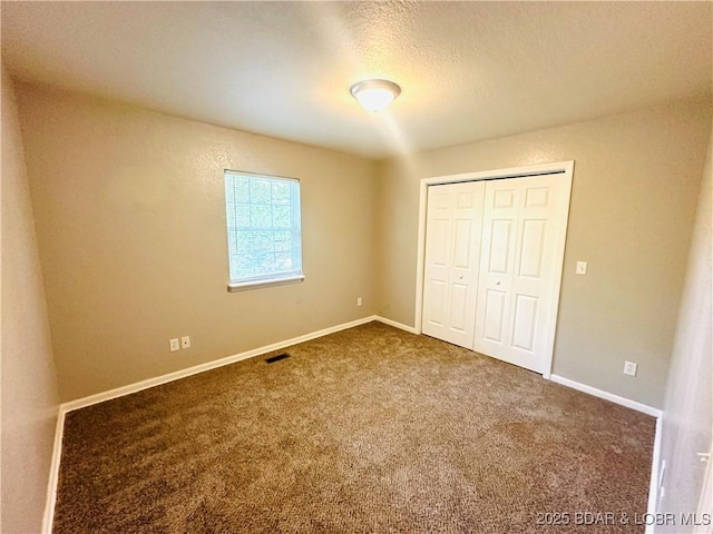 unfurnished bedroom with a textured ceiling, a closet, and dark colored carpet