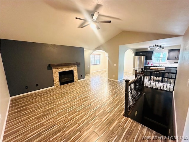 living room with vaulted ceiling, a fireplace, wood-type flooring, rail lighting, and ceiling fan