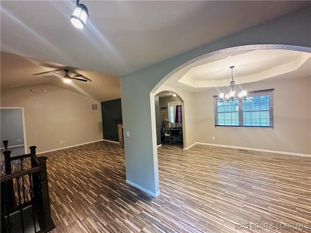 unfurnished living room featuring wood-type flooring, ceiling fan with notable chandelier, and a tray ceiling