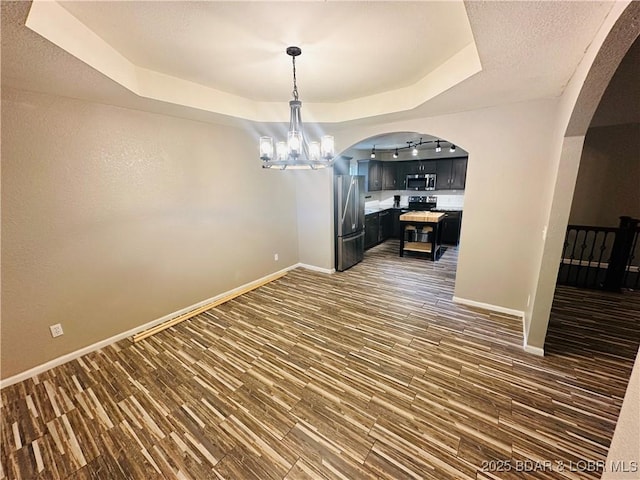 unfurnished dining area with a raised ceiling, dark wood-type flooring, a textured ceiling, and a chandelier