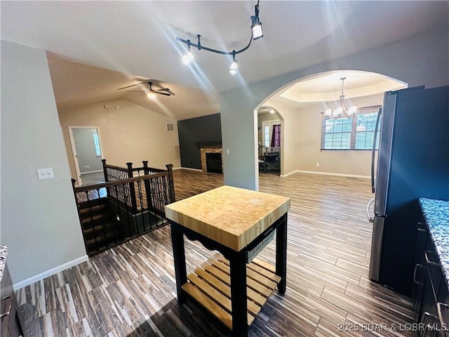 dining space with rail lighting, wood-type flooring, vaulted ceiling, a tray ceiling, and ceiling fan with notable chandelier