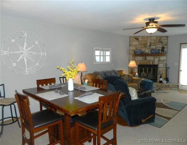 carpeted dining space featuring plenty of natural light, a ceiling fan, and a stone fireplace