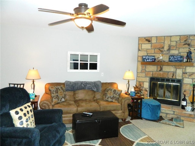 carpeted living room featuring a ceiling fan and a stone fireplace
