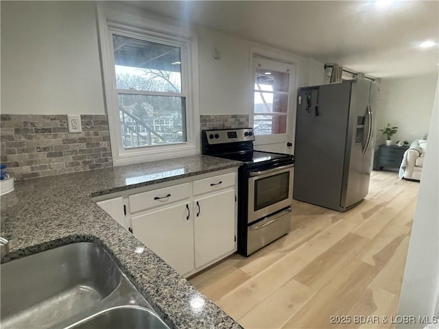 kitchen with stainless steel appliances, tasteful backsplash, light wood-style flooring, white cabinets, and dark stone countertops