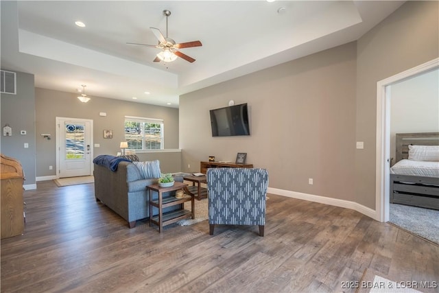 living room featuring dark hardwood / wood-style flooring, a tray ceiling, and ceiling fan