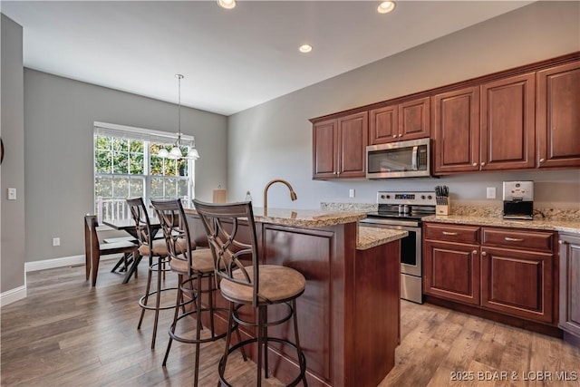 kitchen featuring a kitchen bar, a kitchen island with sink, pendant lighting, stainless steel appliances, and light hardwood / wood-style floors