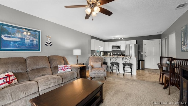 living room featuring ceiling fan, light colored carpet, and a textured ceiling