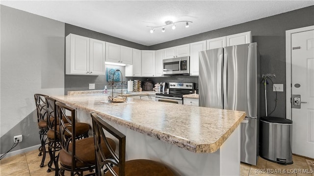 kitchen featuring a kitchen bar, sink, appliances with stainless steel finishes, kitchen peninsula, and white cabinets