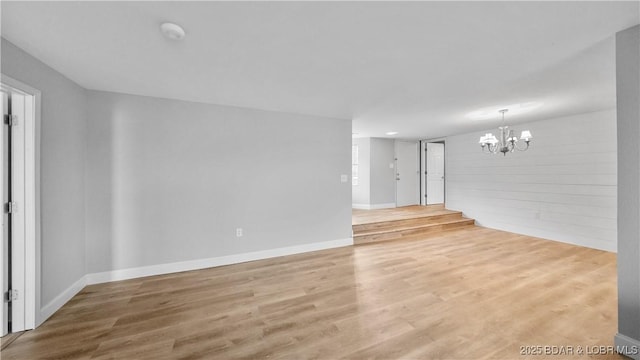 empty room featuring a notable chandelier and light wood-type flooring