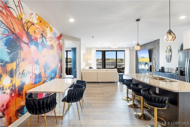 kitchen featuring light stone counters, a breakfast bar, light wood-style floors, white cabinetry, and a sink