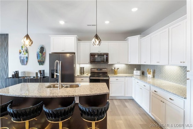 kitchen featuring decorative backsplash, appliances with stainless steel finishes, light wood-style floors, white cabinetry, and a sink